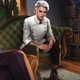 A young woman in a chef's outfit with white hair stares at you from across the room.